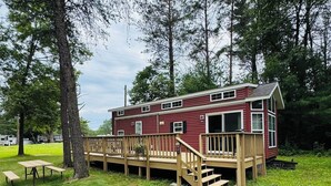 A red cabin with a deck and stairs, surrounded by trees.