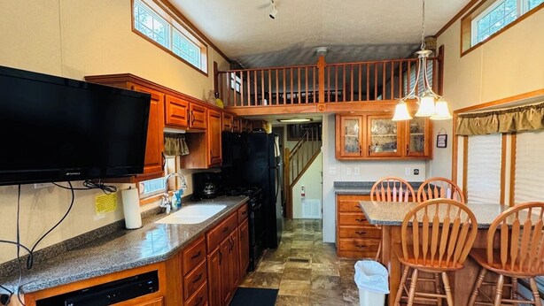 A kitchen with wooden cabinets, a built-in dishwasher, a flat-screen TV, and a dining area with wooden chairs.