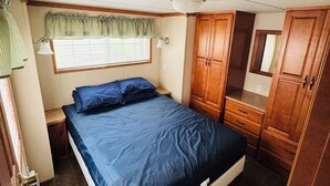A compact bedroom with a single bed, wooden wardrobe, and a small window with a green valance.