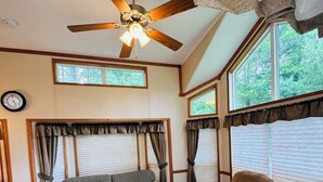A cozy living room with a ceiling fan, two sofas, a coffee table, and large windows with curtains.