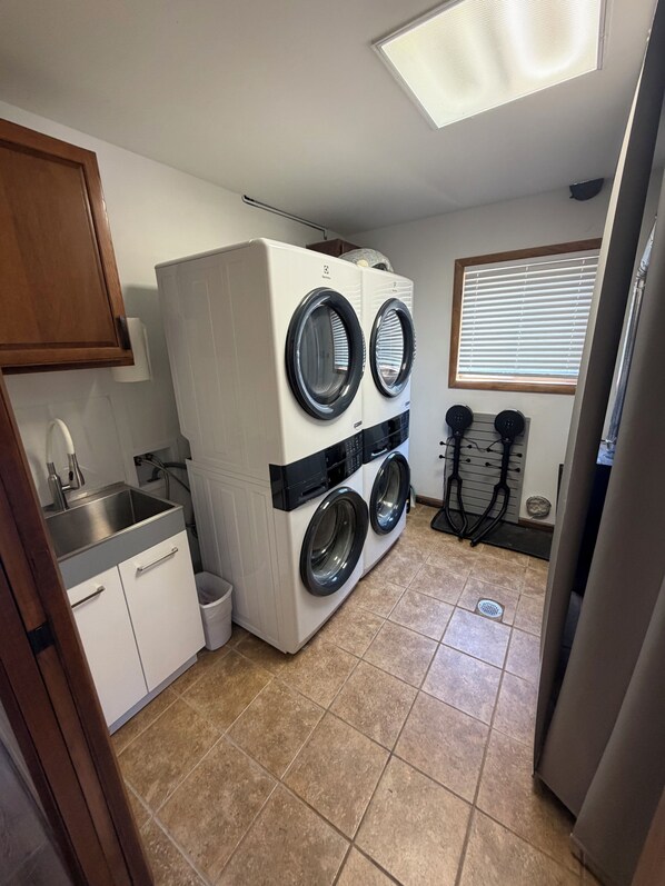 A laundry room with a stacked washer and dryer, a sink, and a window with blinds. - Luxe• Mtn views• Sauna• Hot tub• 2 King Beds• Game Room• Close to Breck (Fairplay)