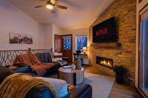 Uma sala de estar aconchegante com lareira, uma TV montada e um ventilador de teto.