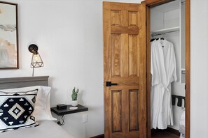 A hotel room with a wooden door, a bedside table with a lamp, a white pillow, a small cactus, and a robe hanging on a rack. - Sauna• Hot tub• 2 King Beds• Game Room• Mtn views• Close to Breck• Pet friendly (Fairplay)