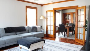 Een woonkamer met een bank, een poef en een eethoek met stoelen en een tafel.