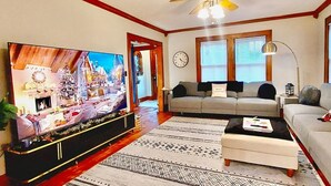 Een woonkamer met een grote flatscreen televisie, een bank, een salontafel en een kamerbreed tapijt met een patroon.