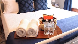 Een netjes opgemaakt bed met kussens, een dienblad met handdoeken en flessen water, en een mandje met toiletartikelen.