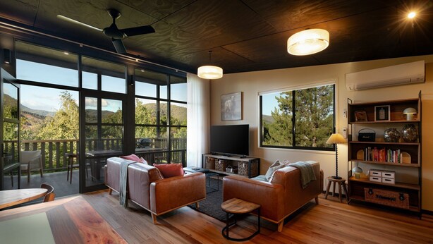 A spacious living room with large windows, a ceiling fan, and a television. - Ned's Bright - Total Luxury (Bright)