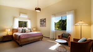 A bedroom with a bed, bedside tables, a chair, a round table, and a large window with curtains. - Ned's Bright - Total Luxury (Bright)