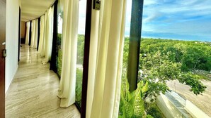 A corridor with large windows and curtains, leading to a room with a view of a green landscape. - Chic 2-bedroom penthouse with private pool, gym, WiFi, W/D & Concierge (Tulum)