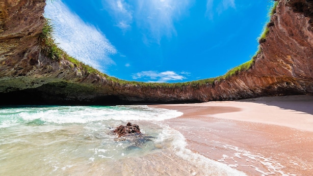 Una playa con agua turquesa cristalina, un acantilado rocoso y una orilla arenosa.