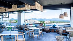 Un restaurante en la azotea con mesas al aire libre, vistas de la ciudad y montañas al fondo.