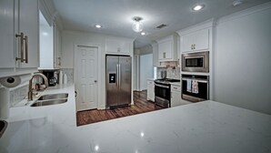 A modern kitchen with white cabinetry, stainless steel appliances, and a marble countertop. - The Game Palace @ Sugar Magnolia (Jackson)