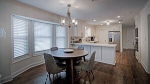 A modern kitchen with a round dining table, grey chairs, and a chandelier. - The Game Palace @ Sugar Magnolia (Jackson)