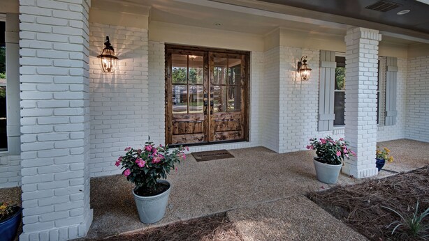 A white brick house with a wooden door, two potted plants, and two wall-mounted lights. - The Game Palace @ Sugar Magnolia (Jackson)