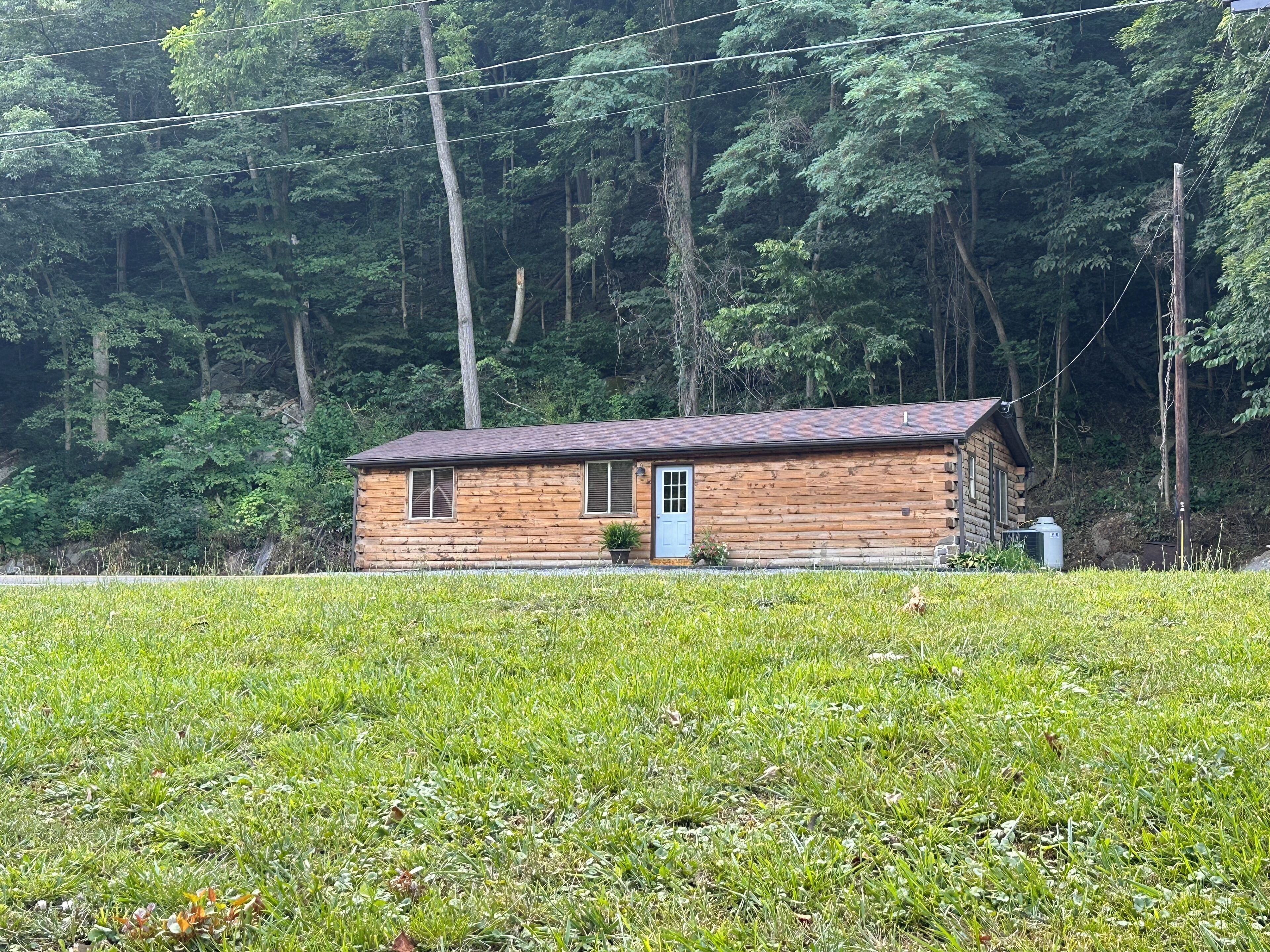 Une petite cabane en bois, dotée d’une seule porte et d’une seule fenêtre, entourée d’une végétation luxuriante et d’arbres.