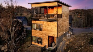 Eine zweistöckige Holzhütte mit einem Balkon im Obergeschoss, einer kleinen Veranda im Erdgeschoss und Blick auf die umliegende Landschaft.