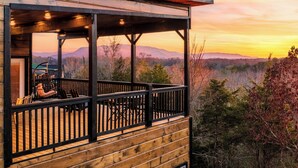 Eine Holzhütte mit einem Balkon mit Blick auf eine gebirgige Landschaft im Sonnenuntergang.