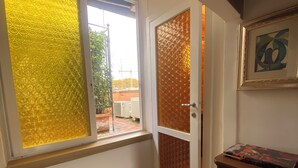 A room with a wooden floor, a window with yellow frosted glass, a door with a brown textured panel, and a framed abstract painting on the wall.