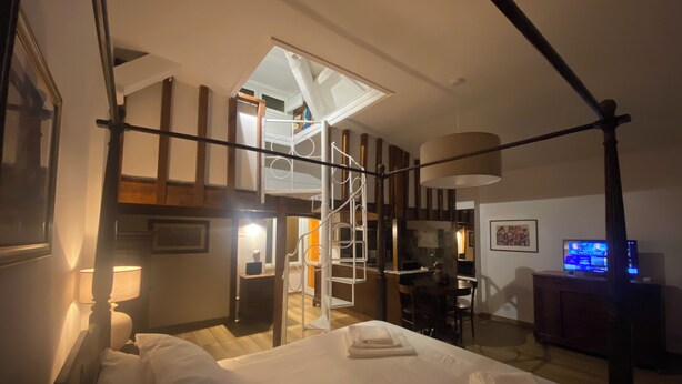 A hotel room with a large bed, a desk, a television, and a staircase leading to an upper level.