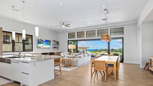 A spacious kitchen with a large island, a dining area with a wooden table and chairs, and a living area with a sofa and a TV. - Amaui Island Escape New 4-bedroom home! Free Access to Mauna Kea & Hapuna Beach! (Kamuela)