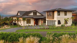 A modern two-story house with a driveway, palm trees, and a view of distant mountains. - Amaui Island Escape New 4-bedroom home! Free Access to Mauna Kea & Hapuna Beach! (Kamuela)