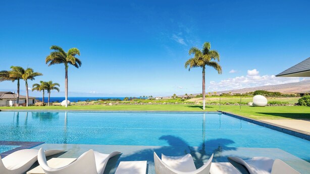 A pool with modern white lounge chairs, palm trees, and a view of the ocean. - Amaui Island Escape New 4-bedroom home! Free Access to Mauna Kea & Hapuna Beach! (Kamuela)