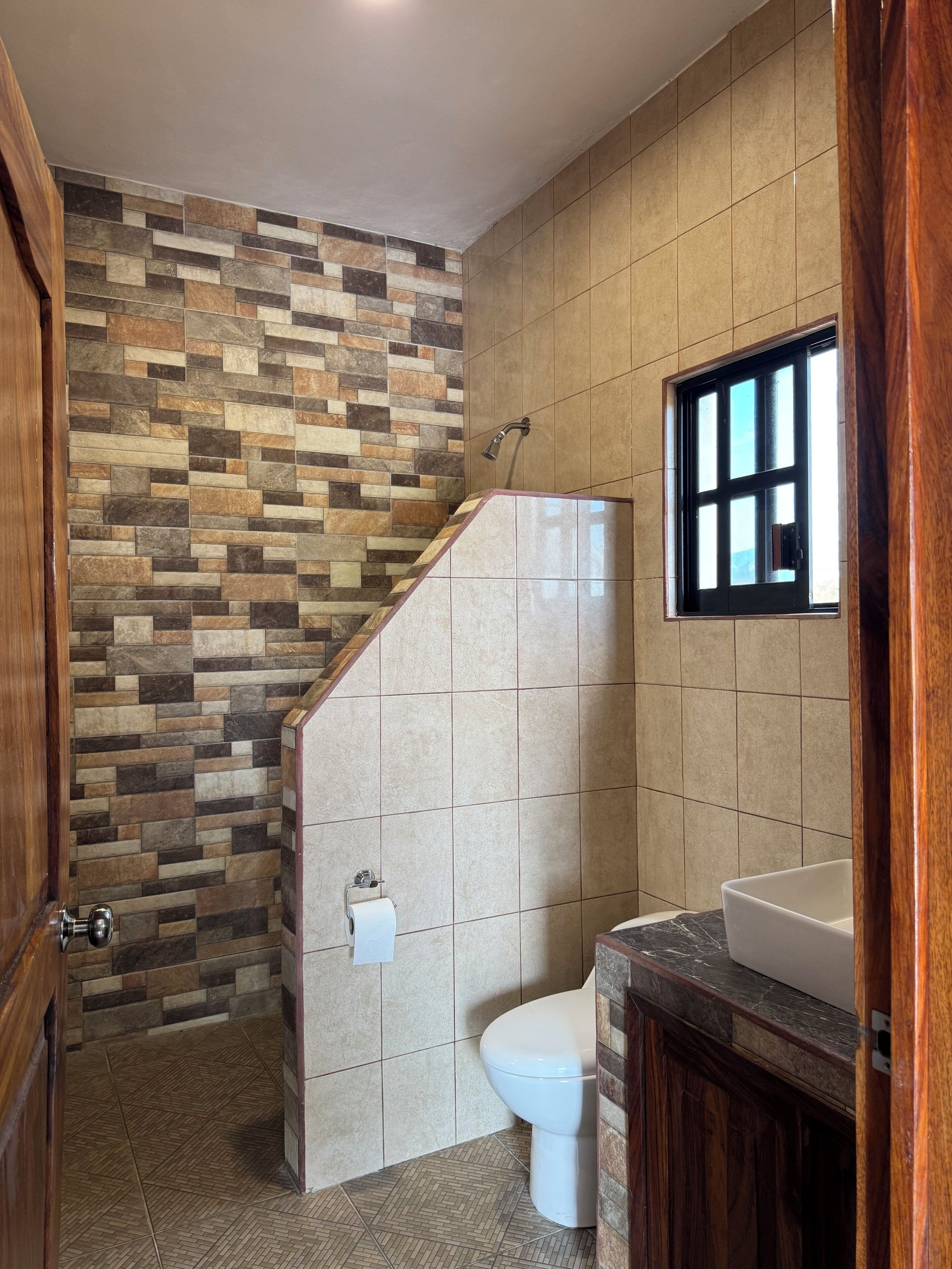 Ein Badezimmer mit gefliestem Duschbereich, Toilette und Waschbecken.