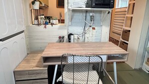 Pieni, käytännöllinen keittiö, jossa on puinen pöytä, metalliverkosta valmistettu tuoli ja punainen matto.