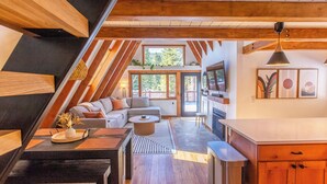 A modern loft-style living space with a loft bed, a sofa, a dining area, and a kitchen. - A-Frame Cabin with Private Sauna & Hot Tub (Breckenridge)