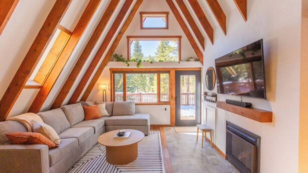 A cozy loft-style living room with a sectional sofa, a coffee table, a fireplace, and a TV mounted on the wall. - A-Frame Cabin with Private Sauna & Hot Tub (Breckenridge)