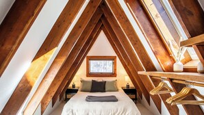 A cozy attic bedroom with a sloped ceiling, a bed with pillows, a nightstand, a window with a view, and wooden beams. - A-Frame Cabin with Private Sauna & Hot Tub (Breckenridge)