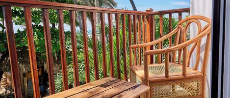 A wooden bench and chair on a balcony with a view of palm trees and a clear sky.