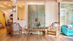 A room with a wooden ceiling, a large rustic door, two wicker chairs, a bench, and a teal sofa. - Aaki Hotel (León)
