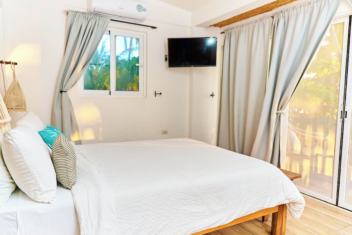 A bedroom with a bed, a TV mounted on the wall, and a window with curtains.
