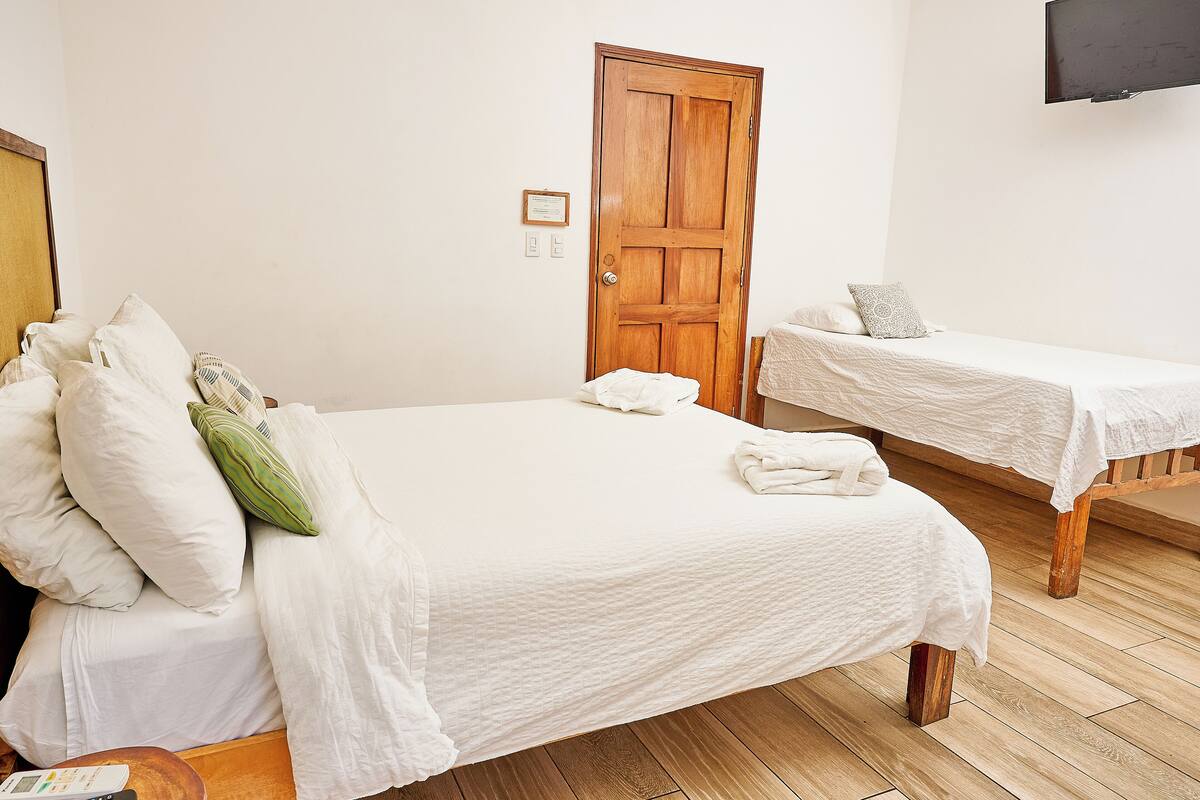 A hotel room with two beds, a wooden door, a flat-screen TV, and a small table with a remote control.