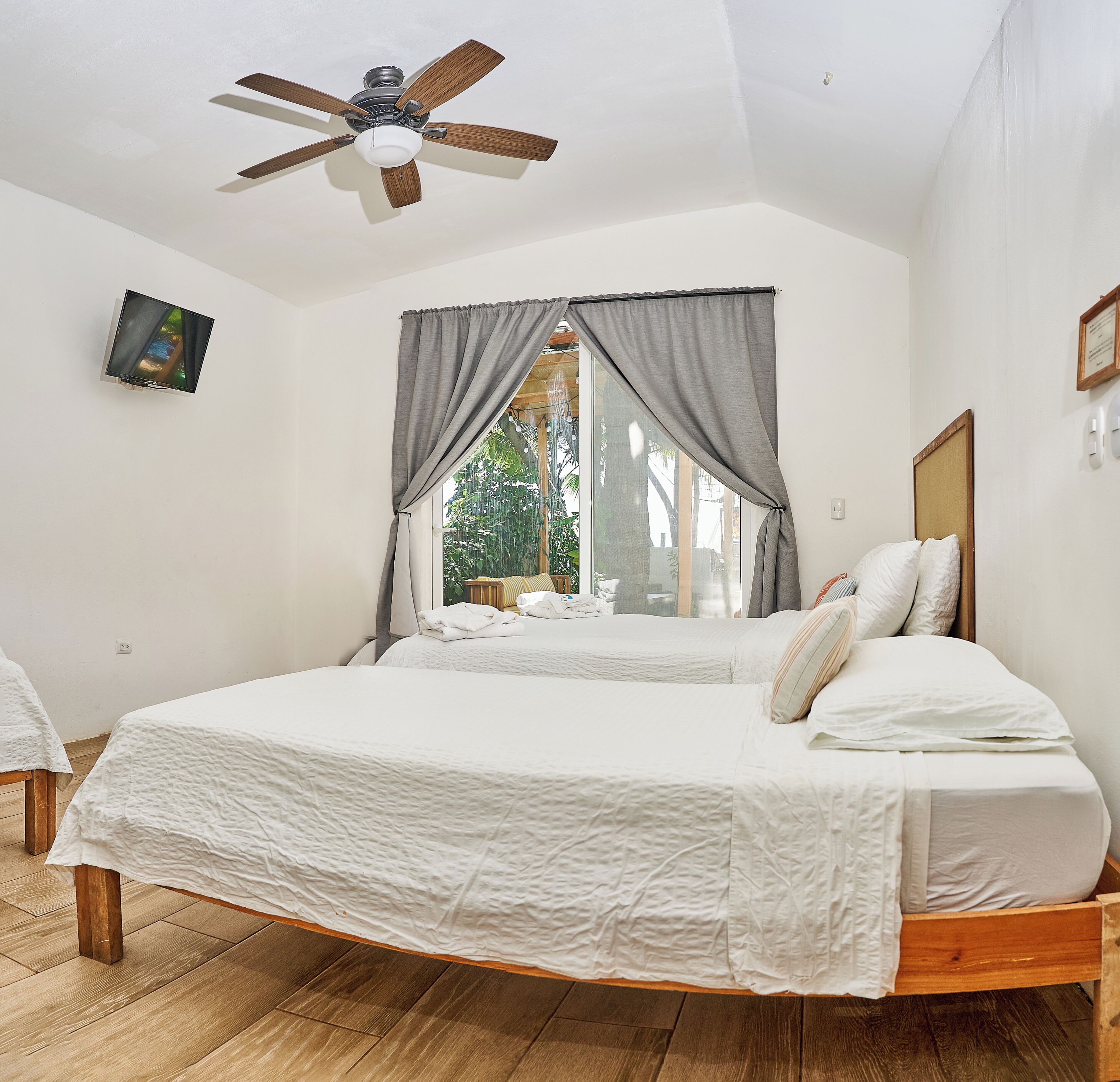 A bedroom with a bed, a ceiling fan, a window with curtains, and a view of greenery outside.