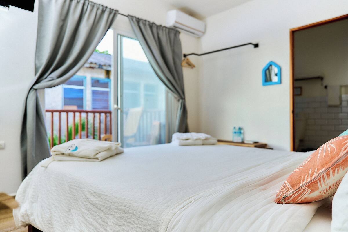 A bedroom with a bed, pillows, a nightstand, and a view of the outside balcony.
