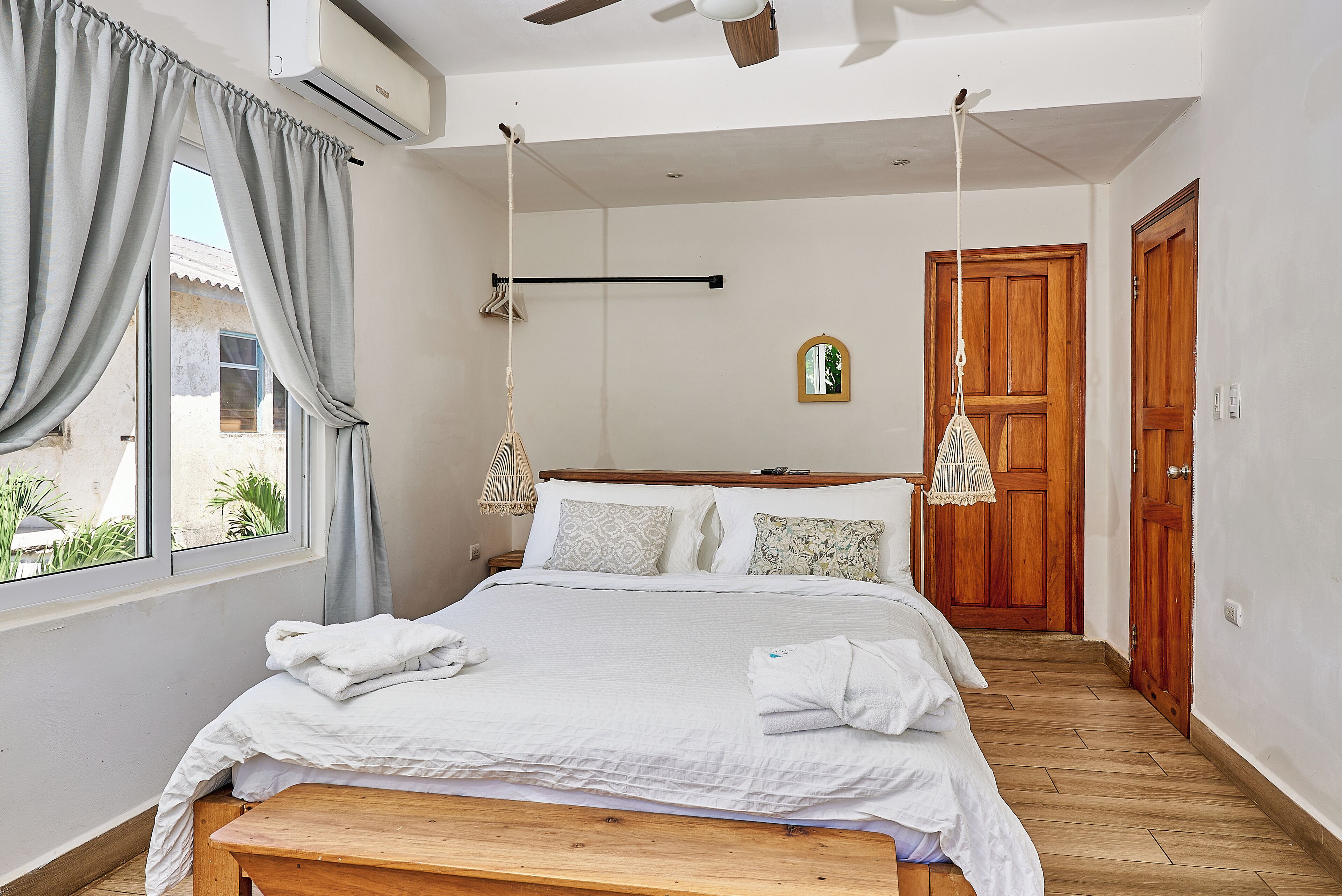 A bedroom with a bed, bedside tables, a hanging light, a wooden door, and a window with curtains.