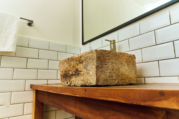 A wooden block on a wooden table in a bathroom with white tiled walls and a mirror above.