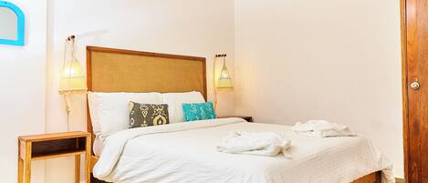 A neatly made bed with white linens and multiple pillows, a wooden nightstand, two wall-mounted lamps, and a wooden door.