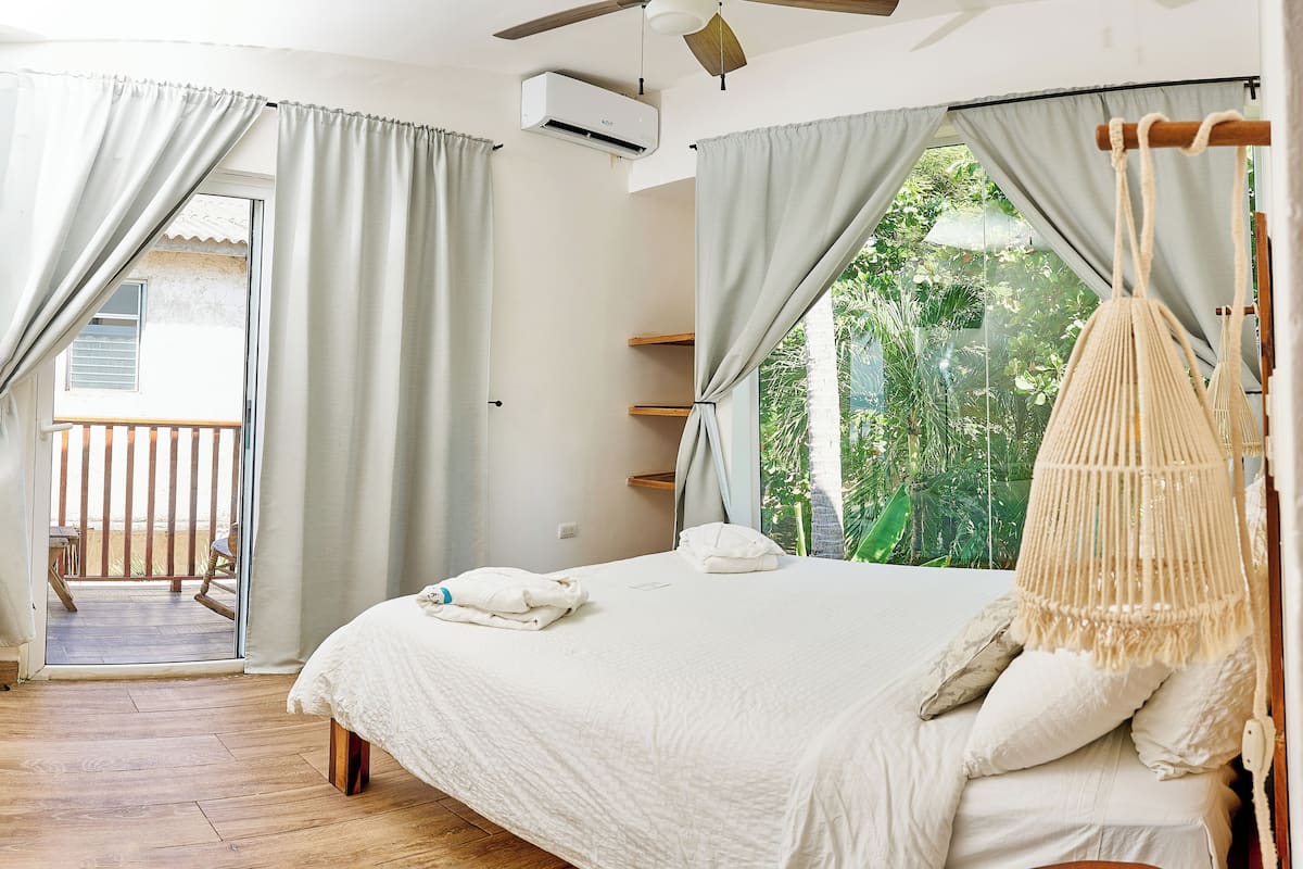A bedroom with a bed, a ceiling fan, and a view of greenery outside.