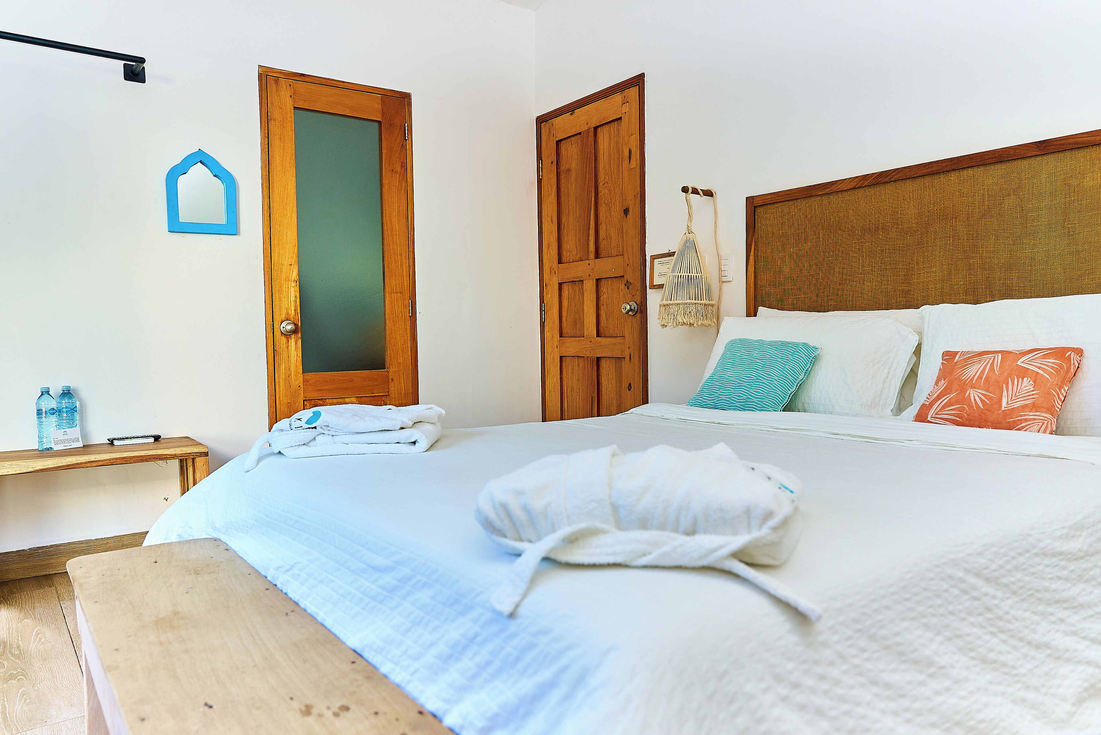 A neatly made bed with a white comforter and a folded bathrobe on it. There is a wooden bench at the foot of the bed.