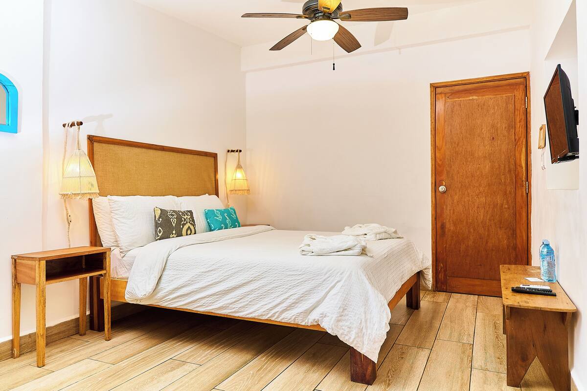 A bedroom with a wooden bed, bedside lamps, a ceiling fan, and a wooden door.