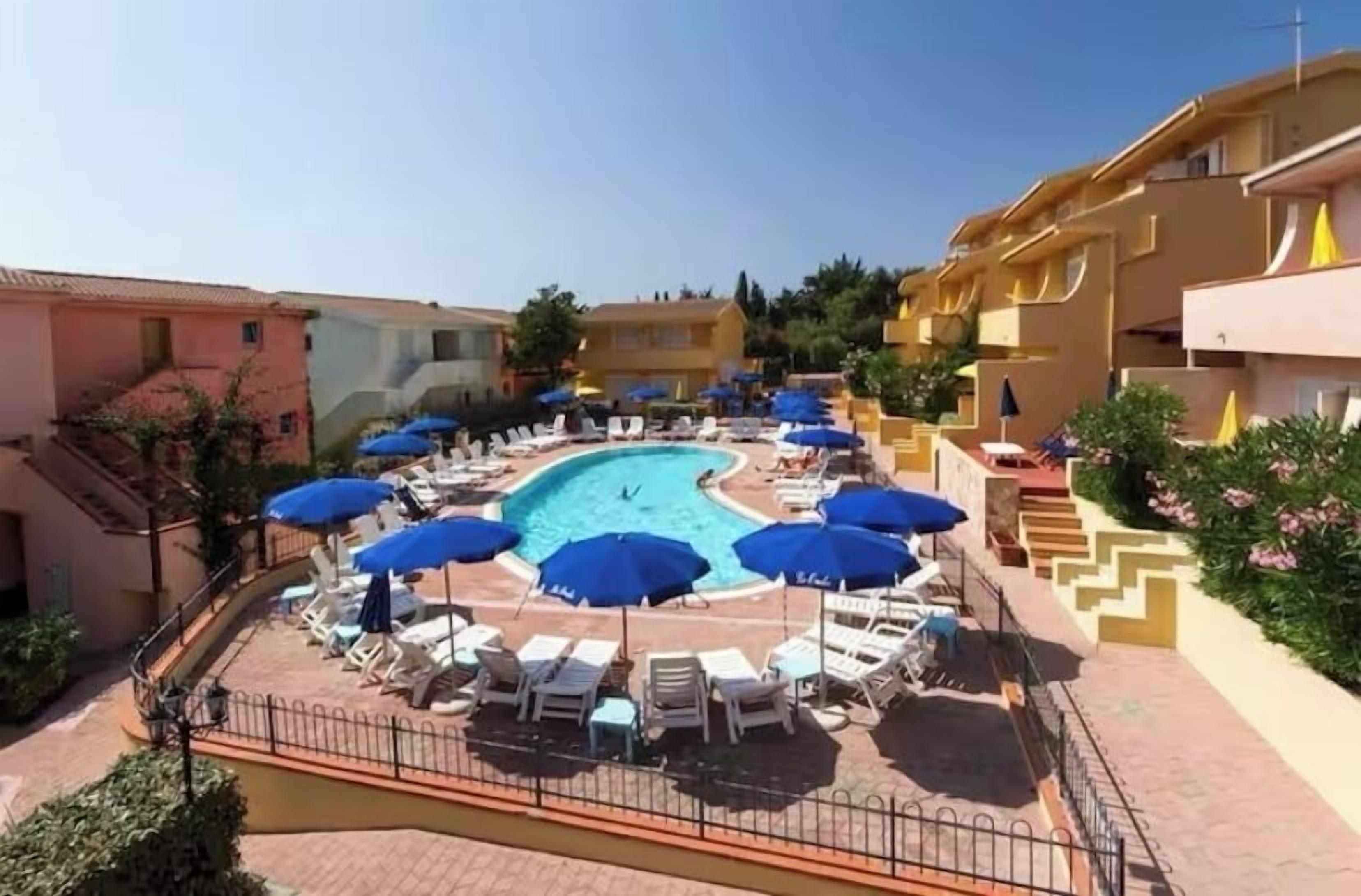 A pool area with lounge chairs and umbrellas, surrounded by buildings with balconies.