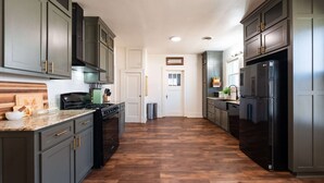 Una cocina con armarios oscuros, un refrigerador negro y piso de madera.