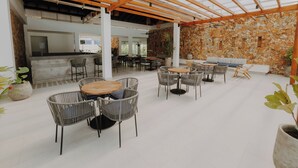 An open-plan restaurant with high ceilings, wooden beams, and a stone wall. Tables and chairs are arranged for dining. - Apartamento en Baia Kristal (Cartagena)