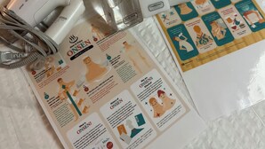 Een badkamer met een witte, geribbelde handdoek, een witte haardroger, twee flesjes douchezeep en een folder op de vloer.