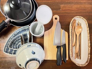 Una cocina equipada con una sartén, una tabla de cortar de madera, un cuchillo, una cuchara y un bol.