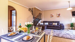 A dining area with a table set for breakfast, a staircase, a living room with a sofa, and a wall with artwork. - 3 bedroom amazing home in Orihuela Costa (Orihuela Costa)
