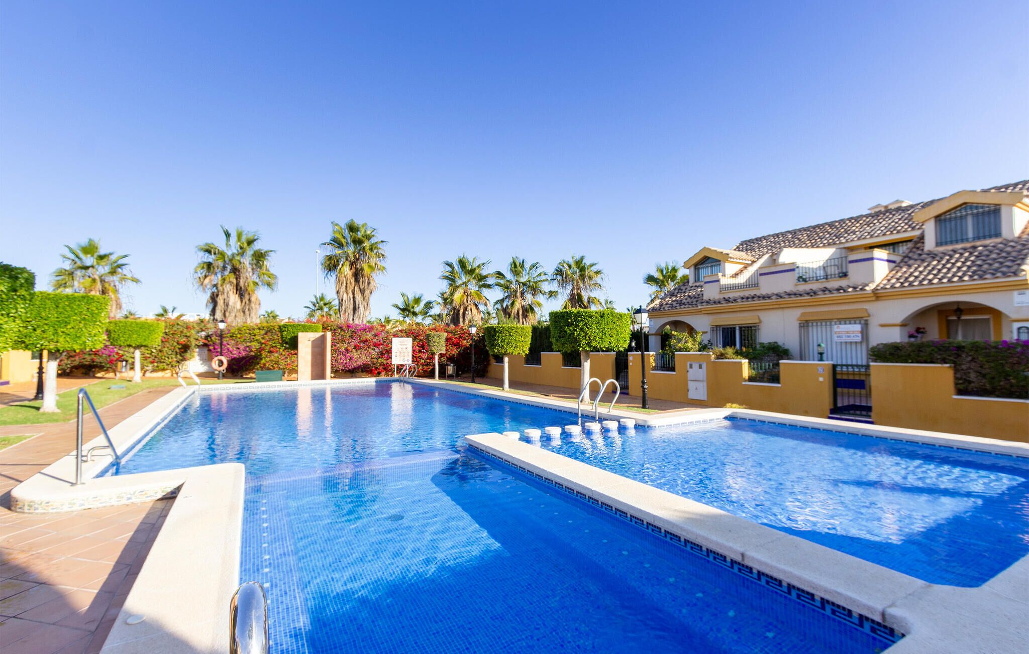 Piscina com superfície de água azul cristalina, rodeada por um calçadão pavimentado.